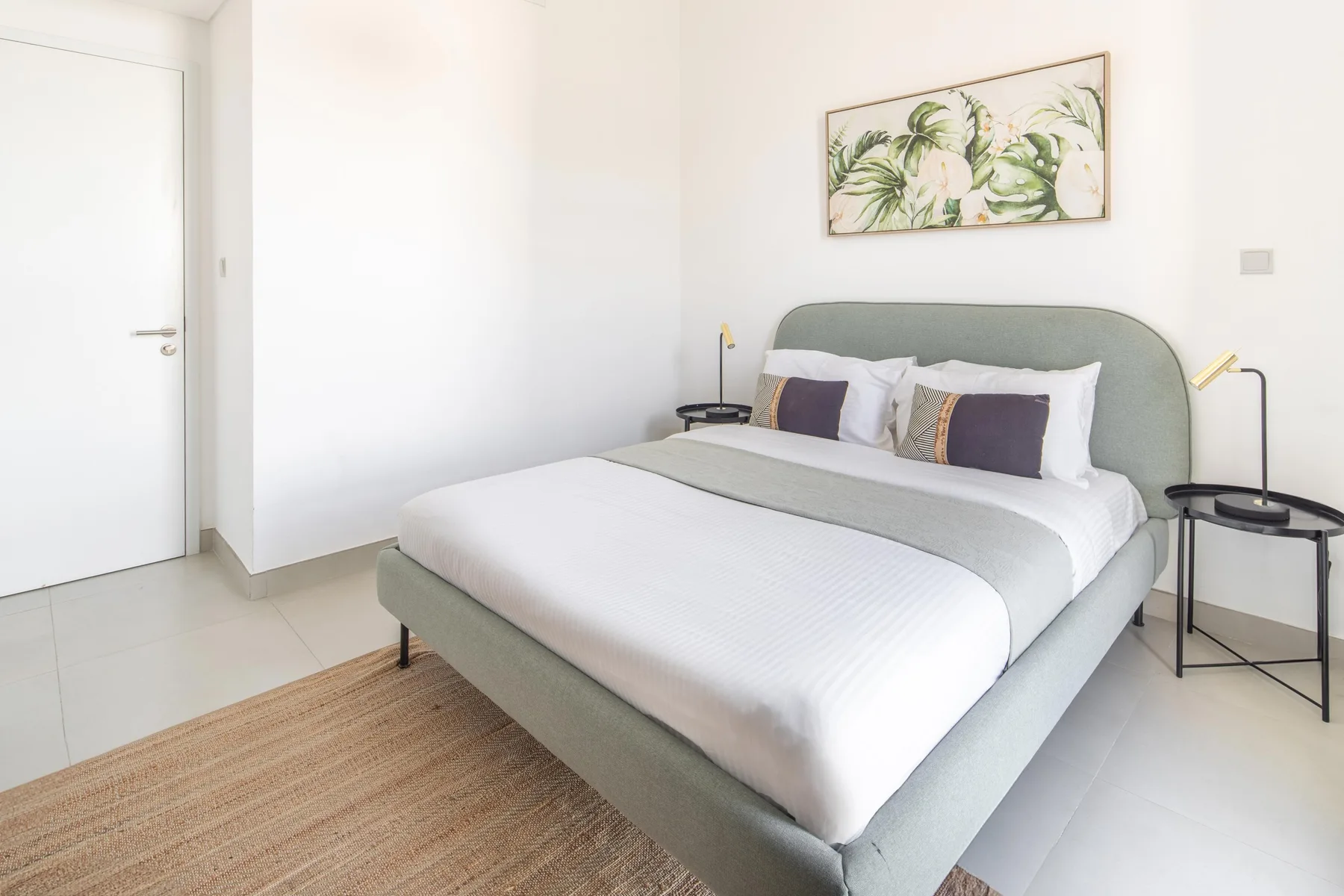 Un dormitorio luminoso con una cama tendida y arte botánico encima.