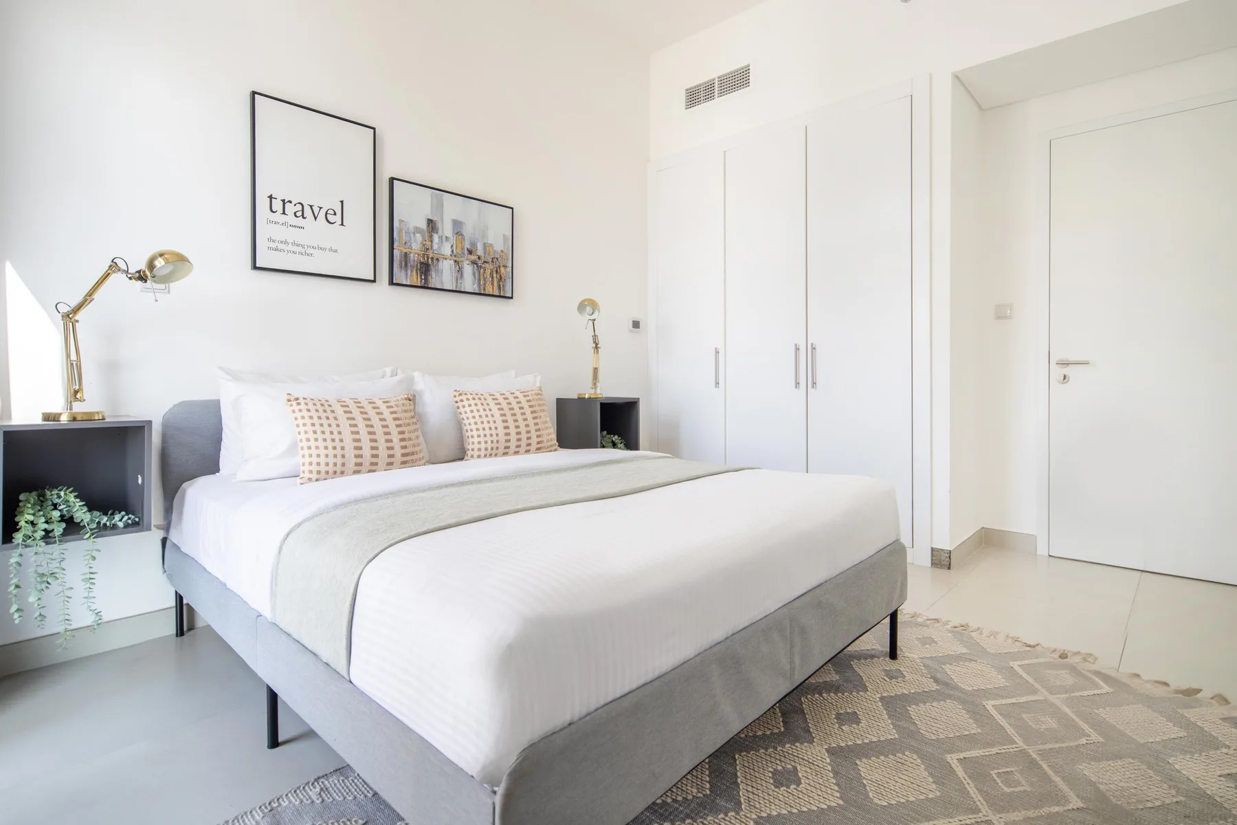 Un dormitorio luminoso con una cama tendida, mesitas de noche y cuadros en la pared.