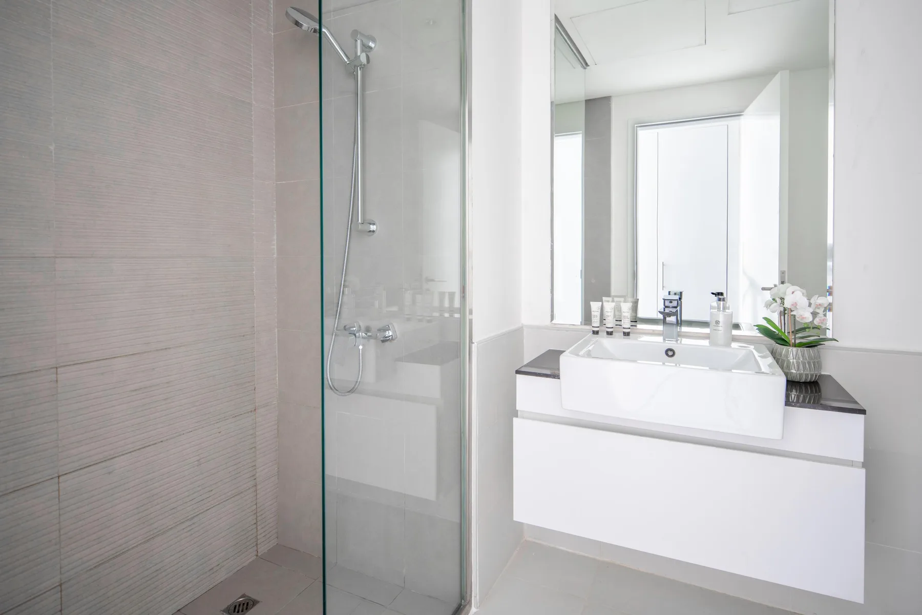Un baño luminoso con ducha de vidrio y un lavabo blanco.