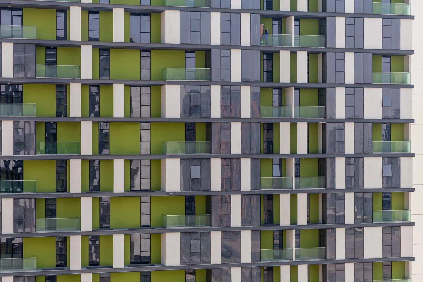 Fachada de un edificio moderno de apartamentos con balcones repetidos y paneles verdes.