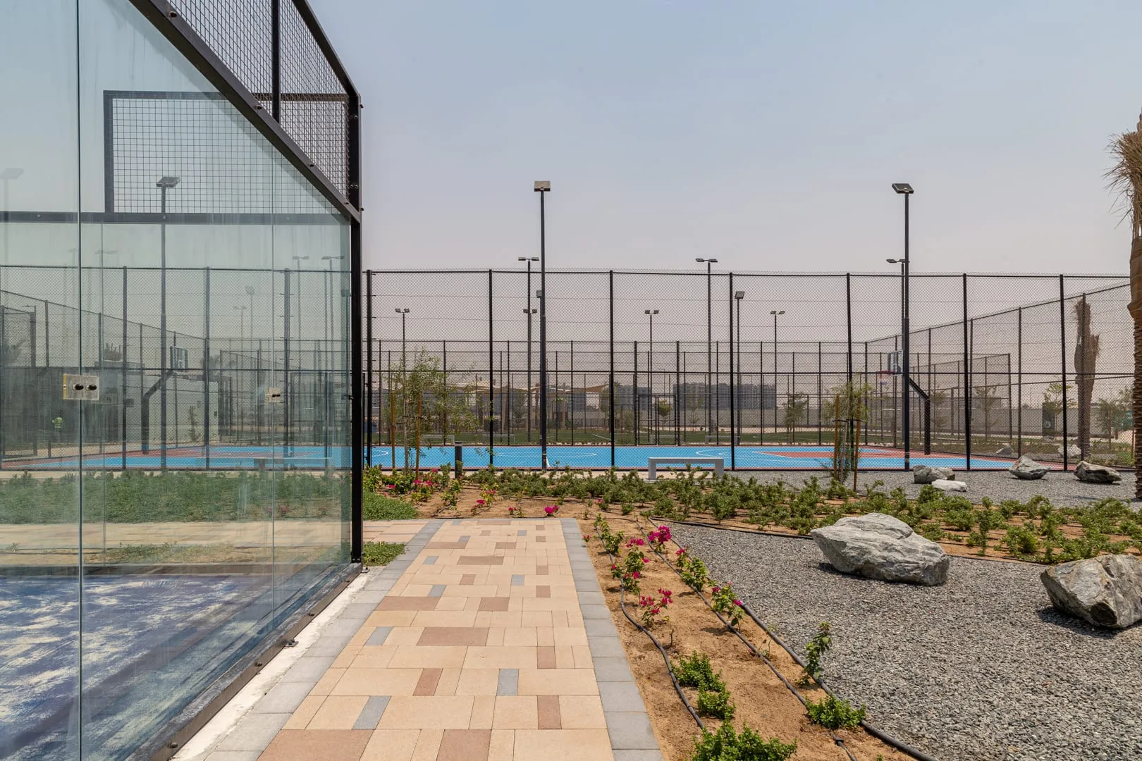 Una pista deportiva al aire libre está cercada junto a un sendero pavimentado.