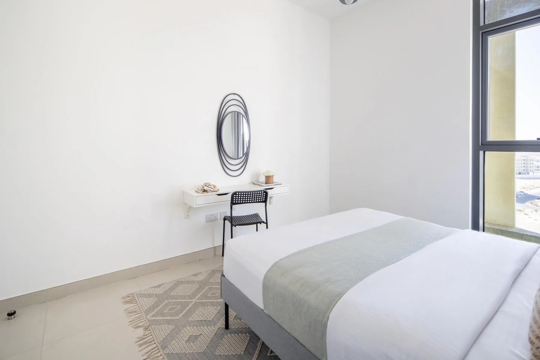 Un dormitorio luminoso con cama, escritorio y una ventana grande.