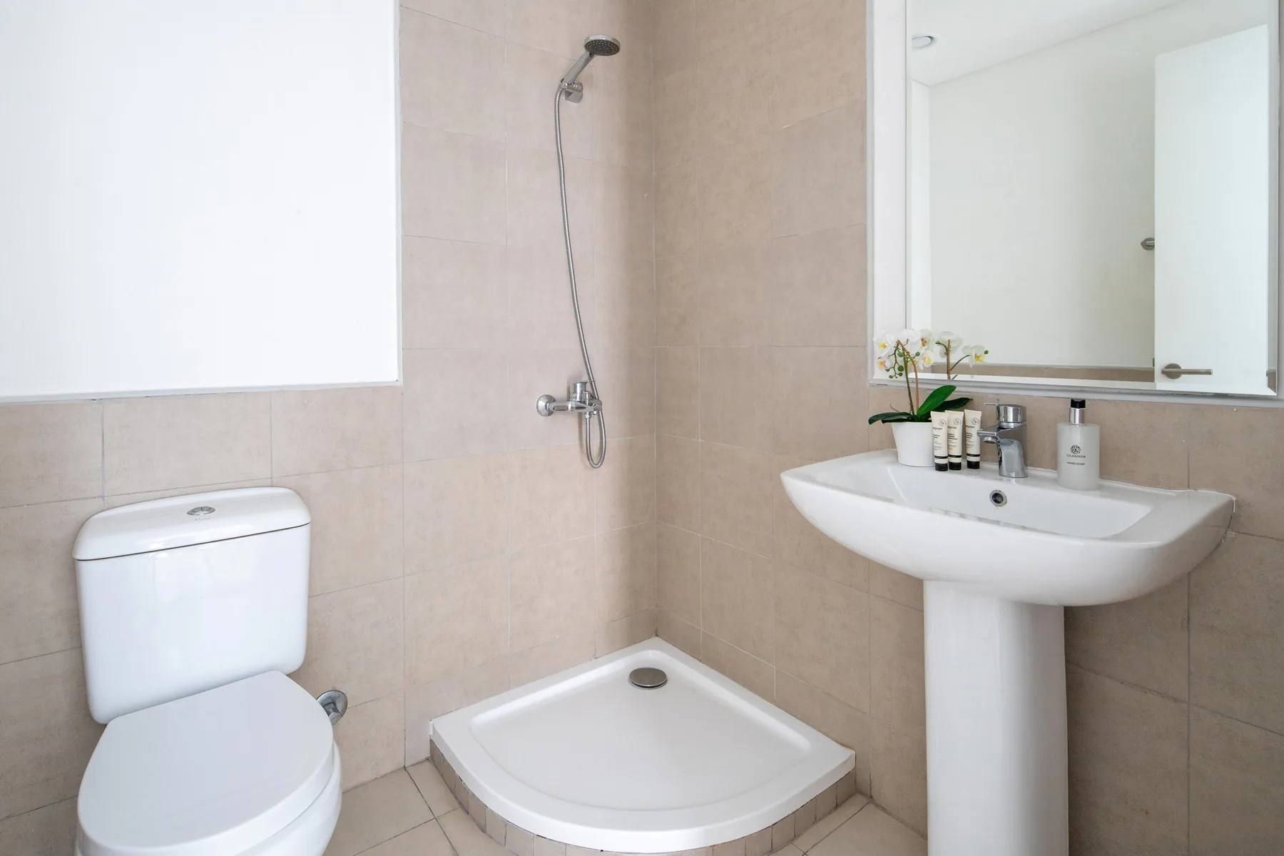 Un baño con ducha, inodoro y lavabo con pedestal.