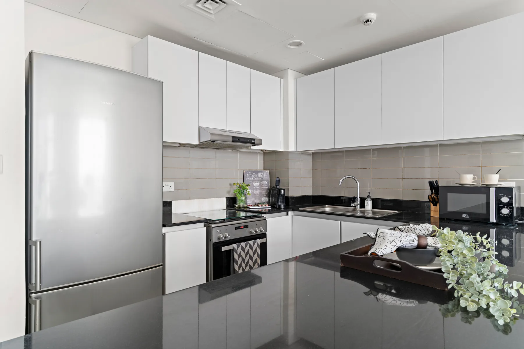 Una cocina moderna con gabinetes blancos, electrodomésticos de acero inoxidable y una encimera oscura.