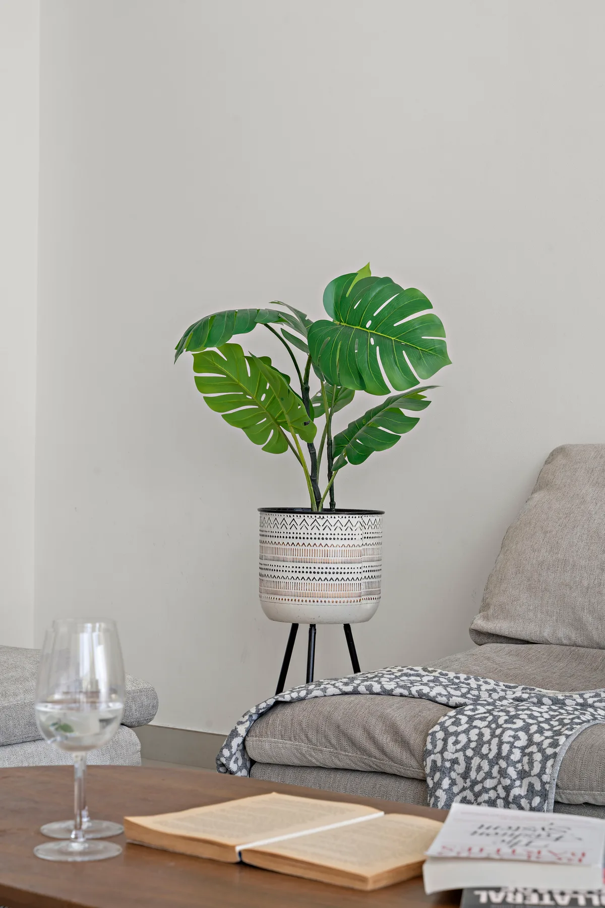 Un rincón de lectura con una planta frondosa junto a un asiento acolchado y un libro abierto.