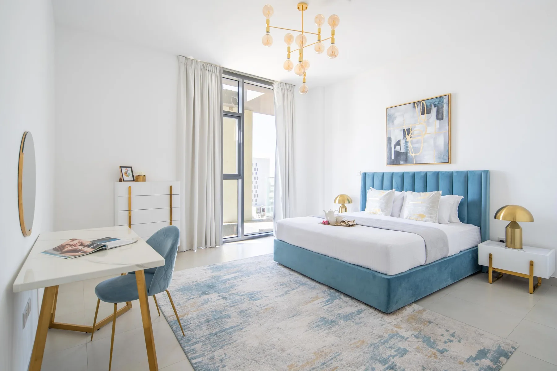 Un dormitorio luminoso con una cama tapizada en color turquesa y un escritorio junto a la ventana.