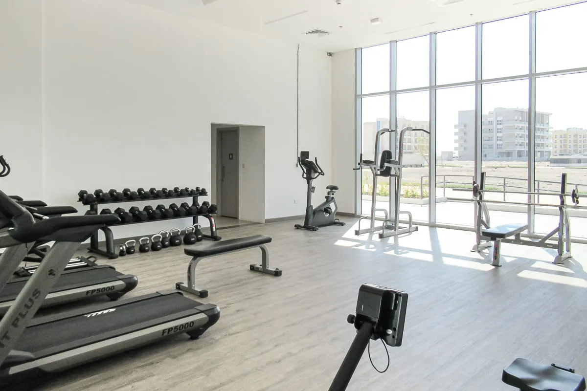 Un gimnasio luminoso con equipo de ejercicio y grandes ventanales.