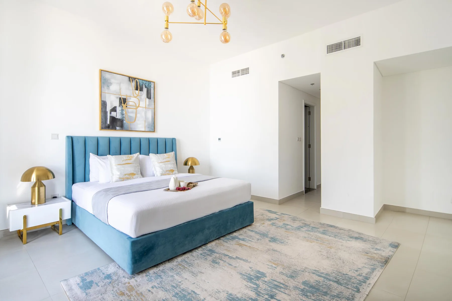 Un dormitorio luminoso con una cama tapizada azul y una alfombra grande.