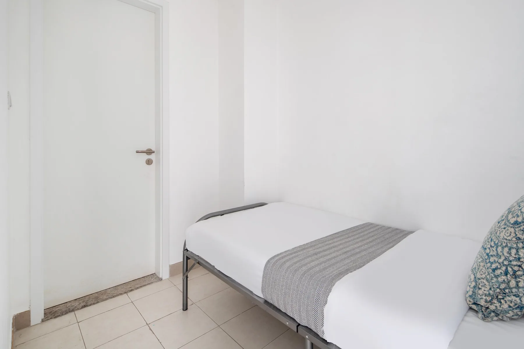 Un dormitorio con una cama vestida de blanco y una manta gris.