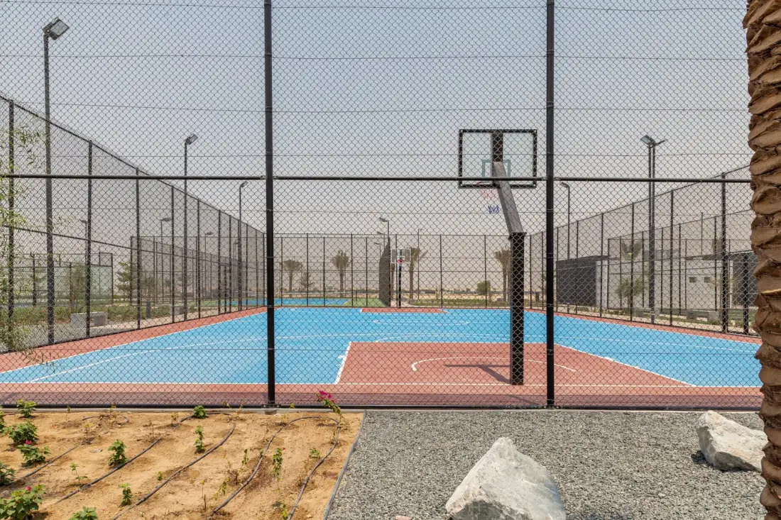 Una cancha de baloncesto al aire libre con superficie azul y cercado perimetral.
