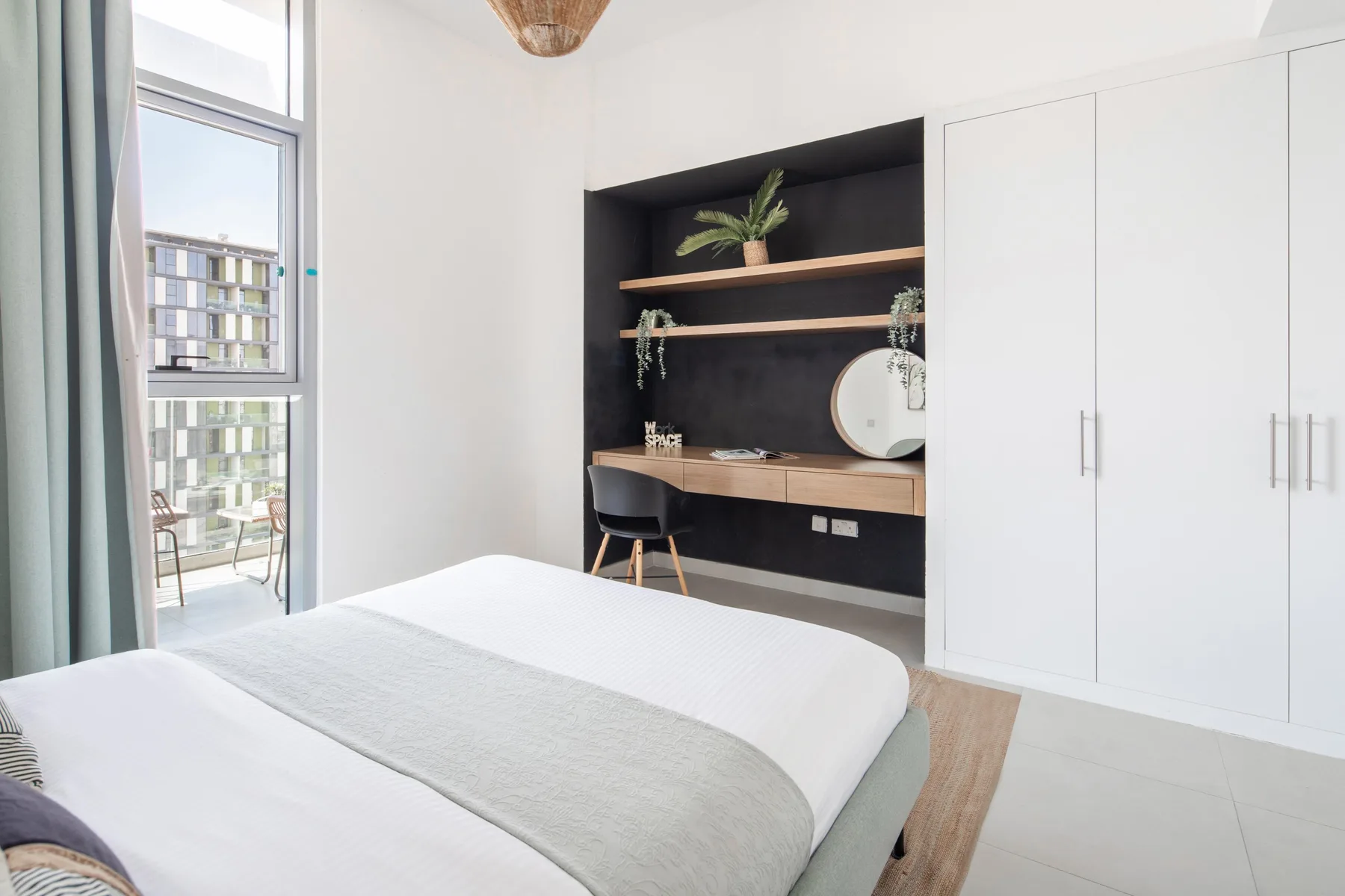 Un dormitorio luminoso con cama, escritorio empotrado y grandes ventanas.