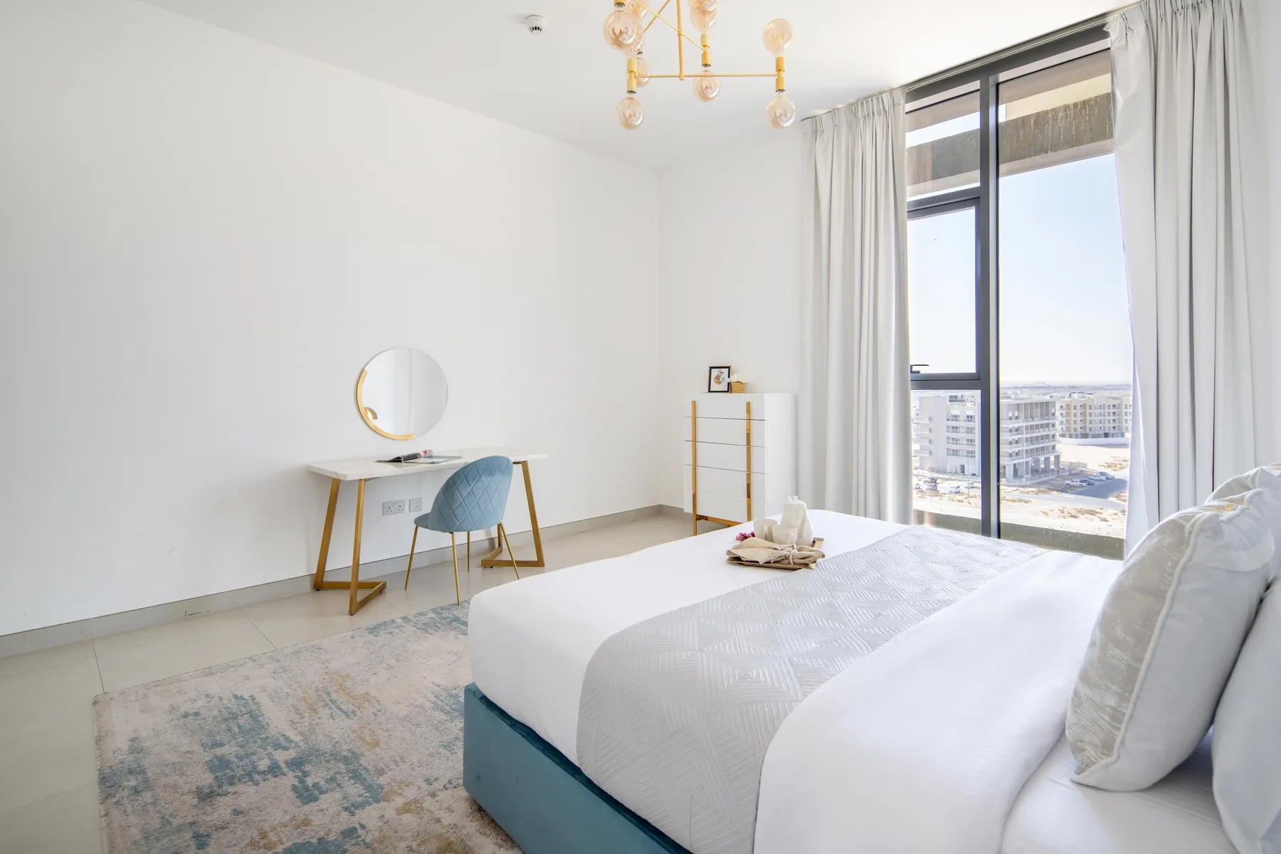 Un dormitorio luminoso con una cama, un escritorio pequeño y una ventana grande.
