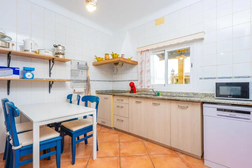 A bright kitchen with a dining table, blue chairs, and a long countertop.