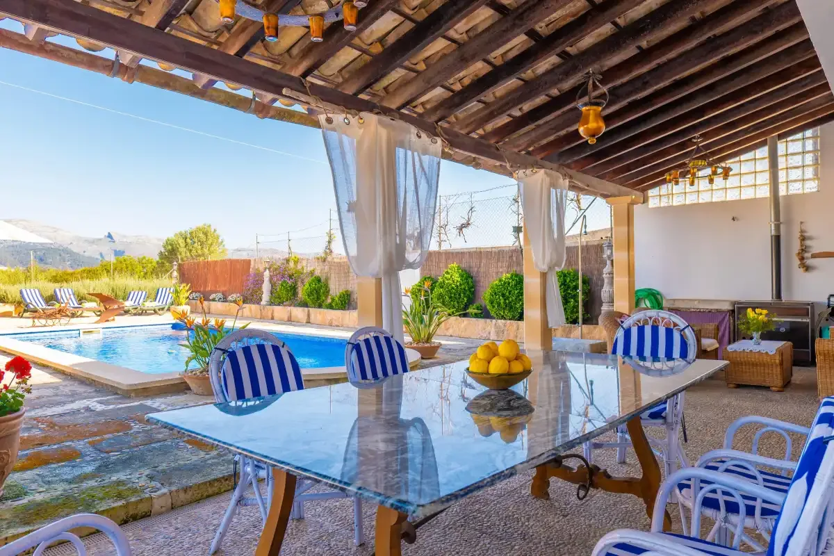 A covered outdoor dining area overlooks a swimming pool and garden.