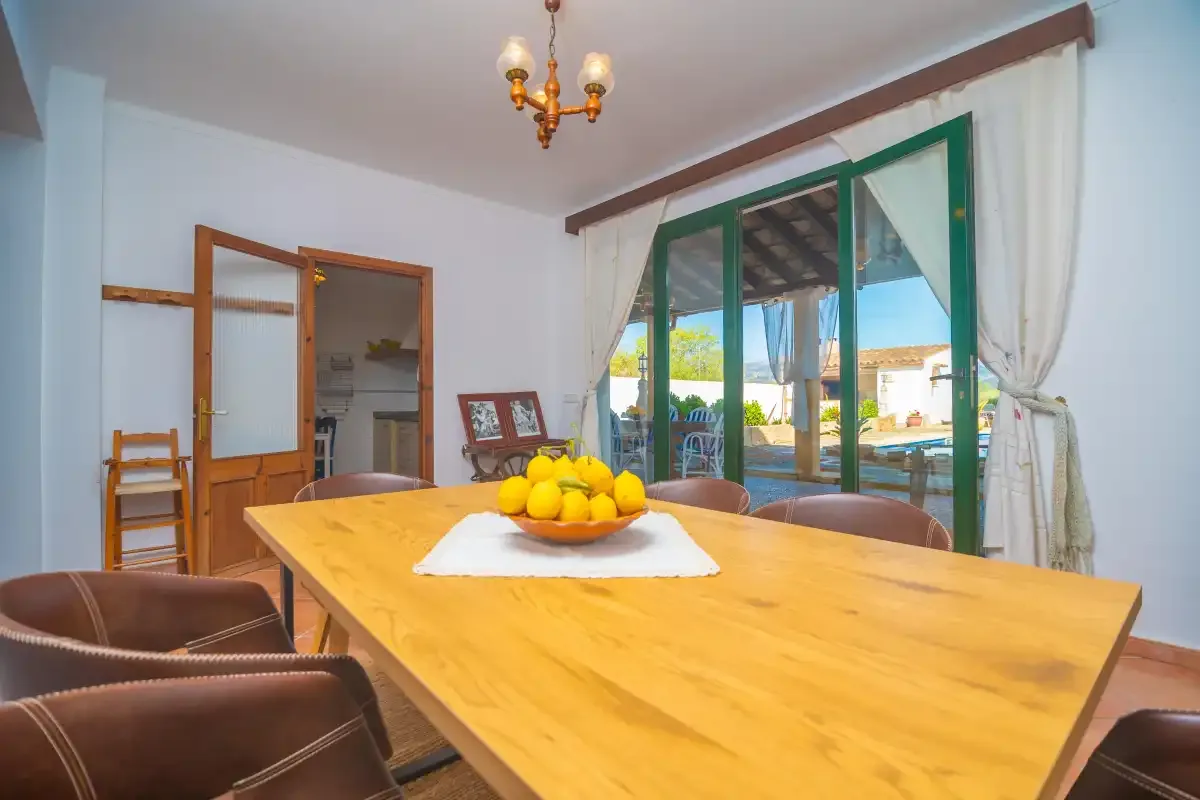A dining room with a long wooden table and glass doors opening onto a patio.