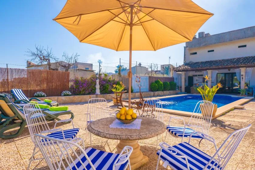 An outdoor poolside seating area with striped chairs beneath a large yellow umbrella.