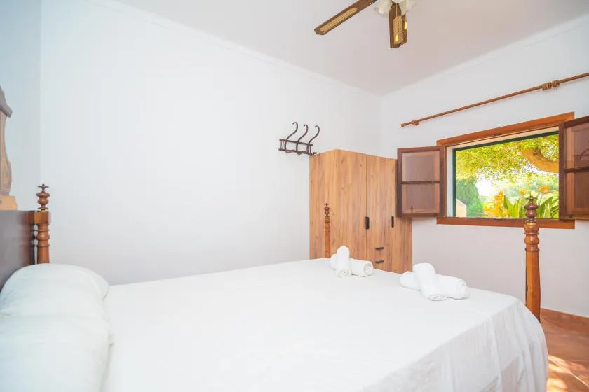A bright bedroom with white bedding and an open window overlooking greenery.