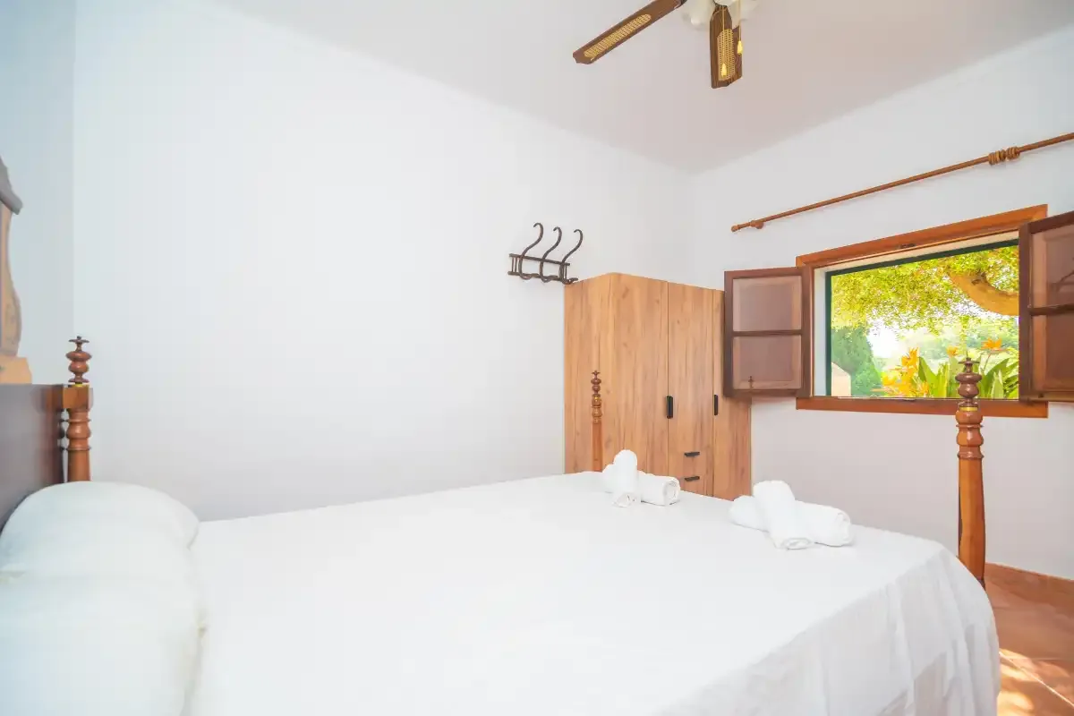 A bedroom with a neatly made bed and an open window overlooking greenery.