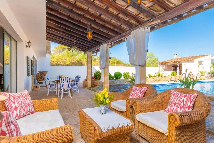 A covered outdoor patio with wicker seating overlooks a swimming pool.