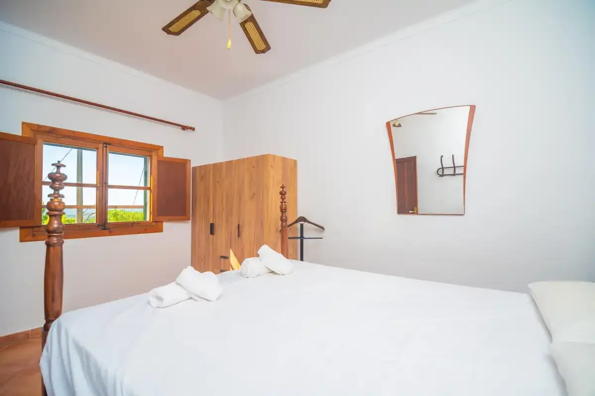 A bedroom with a bed, wooden wardrobe, and open window.
