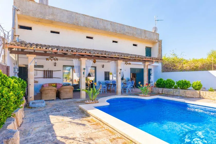 A swimming pool sits beside a covered patio with outdoor seating.