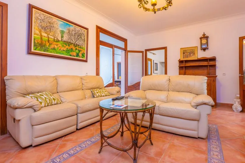 A living room with light-colored seating, a glass coffee table, and framed artwork.