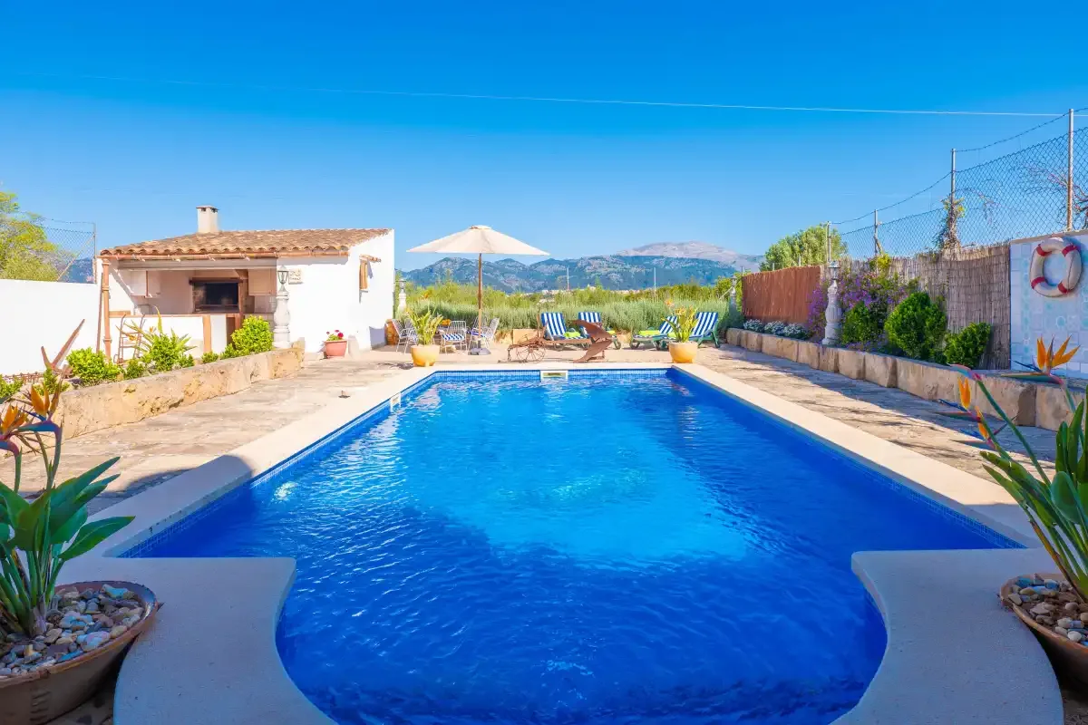 An outdoor swimming pool sits beside a paved patio and a small building.