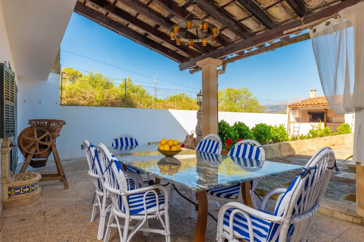A covered outdoor dining area has a table surrounded by blue-and-white striped seating.