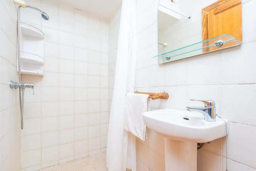 A bright tiled bathroom with a shower, sink, and wall mirror.