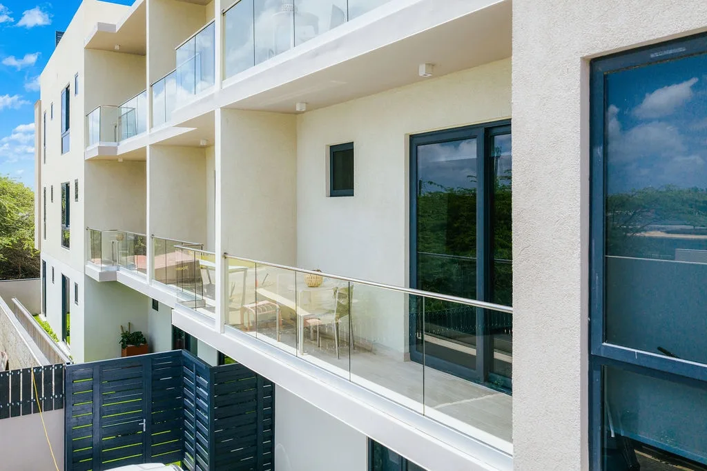 The property features modern balconies with sleek glass railings and outdoor seating, creating a bright and airy atmosphere under clear blue skies.