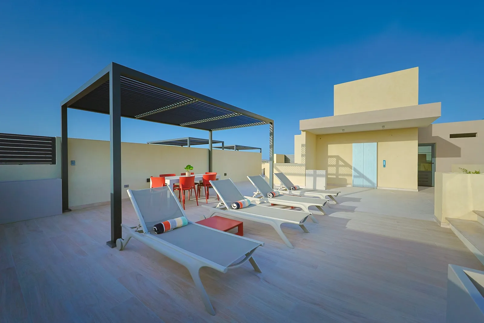 Modern rooftop terrace featuring sun loungers and a shaded dining area set against a bright blue sky—the perfect spot to unwind in style.