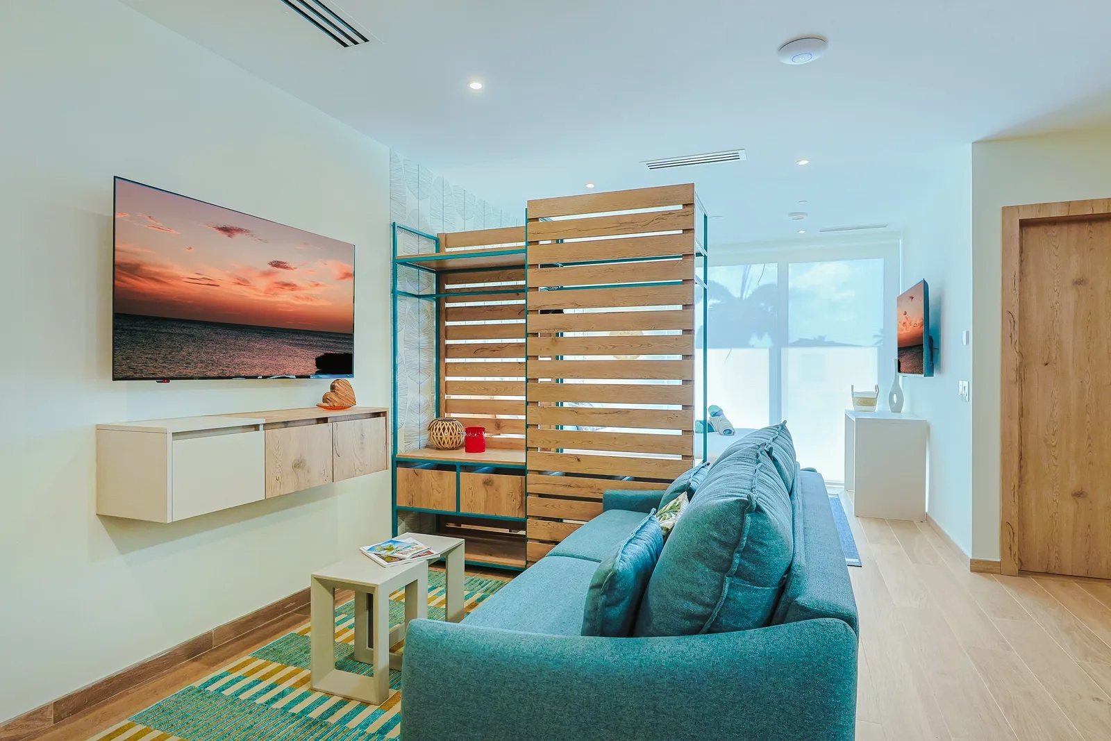 Your modern beach-themed living space awaits, with coastal-inspired decor, a wooden room divider, and a comfortable seating area. Relax by the large TV or gather around the inviting teal sofa after sun-filled days.