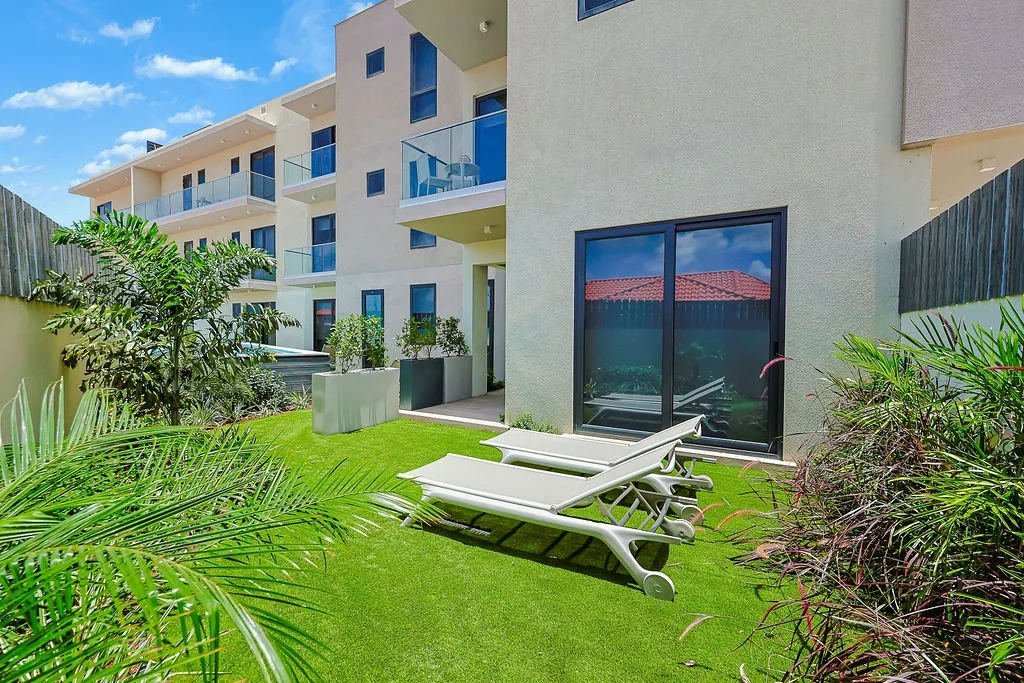 Beautifully landscaped outdoor space with comfortable loungers, lush greenery, and a modern building backdrop—perfect for relaxing and enjoying the sunny surroundings.