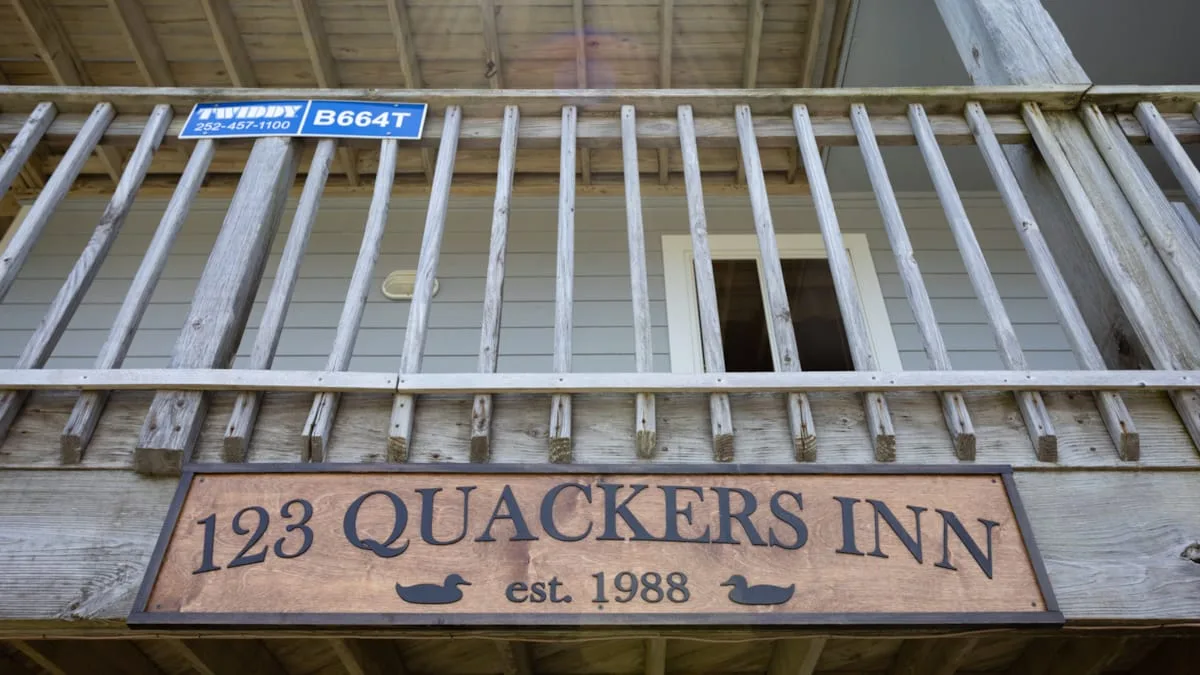 An exterior wooden railing with a sign reading “123 Quackers Inn.”