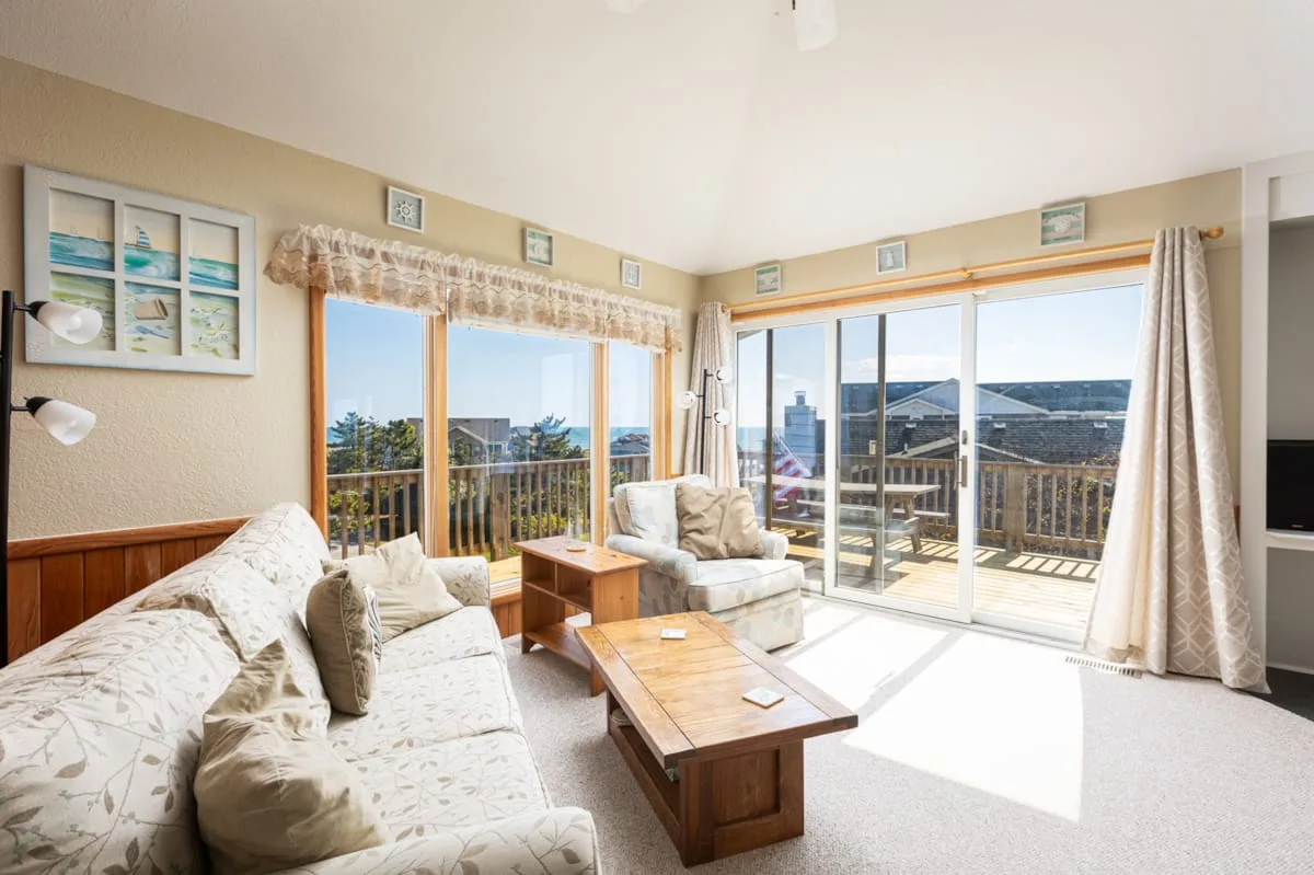 A bright living room with seating and large windows opening onto a balcony.
