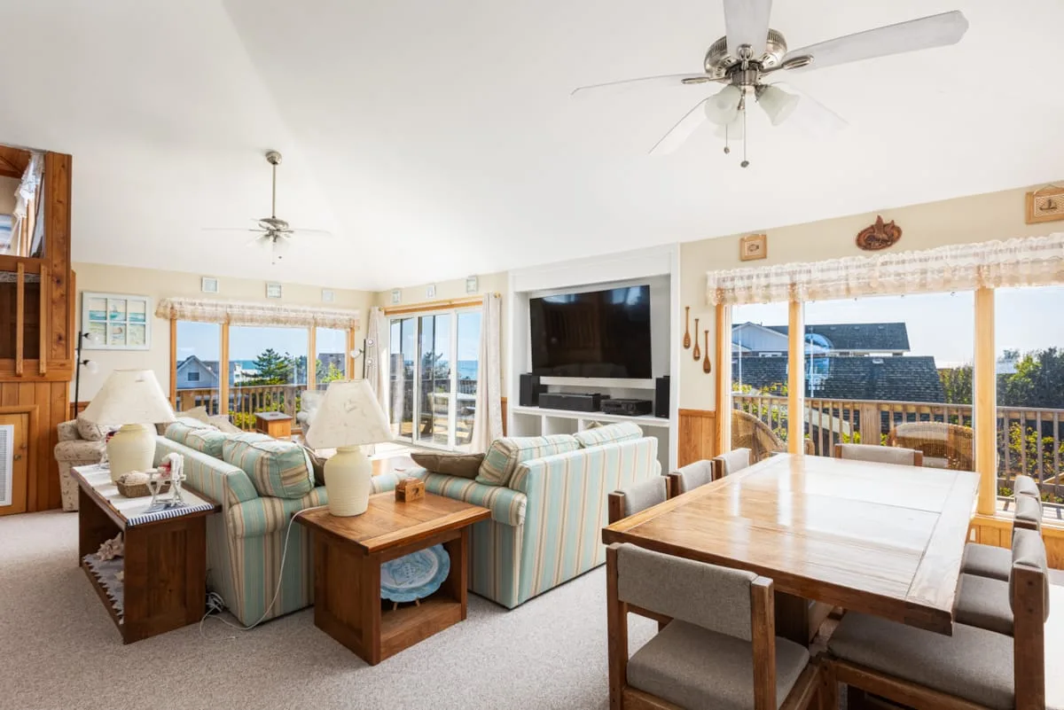 A bright living and dining area has striped seating, a wooden table, and large windows.