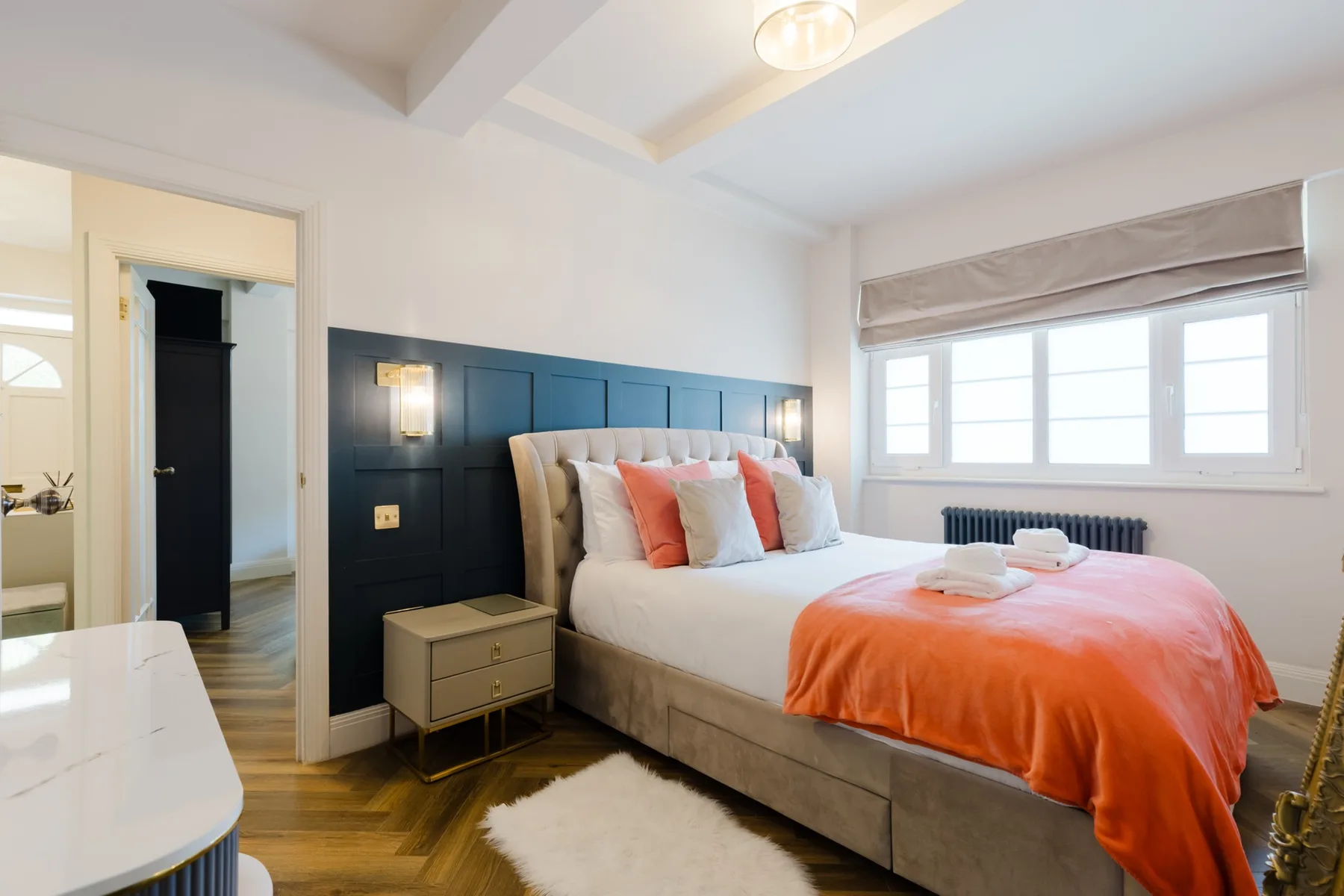 Un dormitorio luminoso con una cama grande, ropa de cama naranja y ventanas amplias.