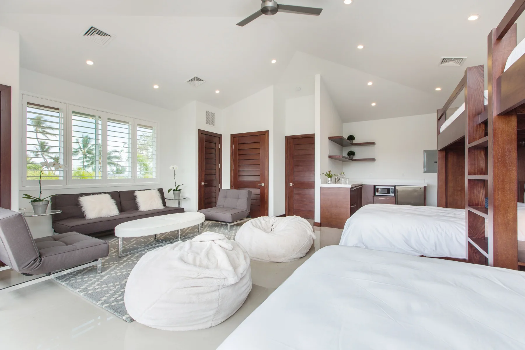 Dormitorio luminoso con zona de estar, cocina pequeña y ventanas grandes.