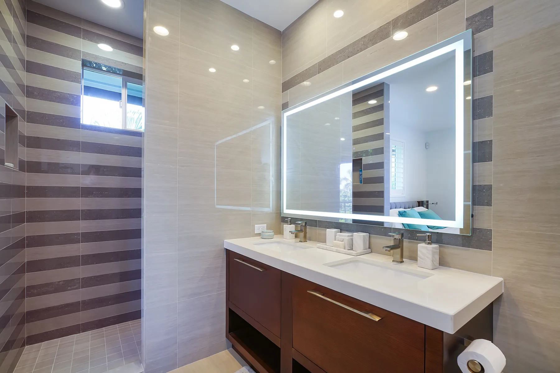 Un tocador de baño con azulejos, un espejo amplio iluminado y una encimera.