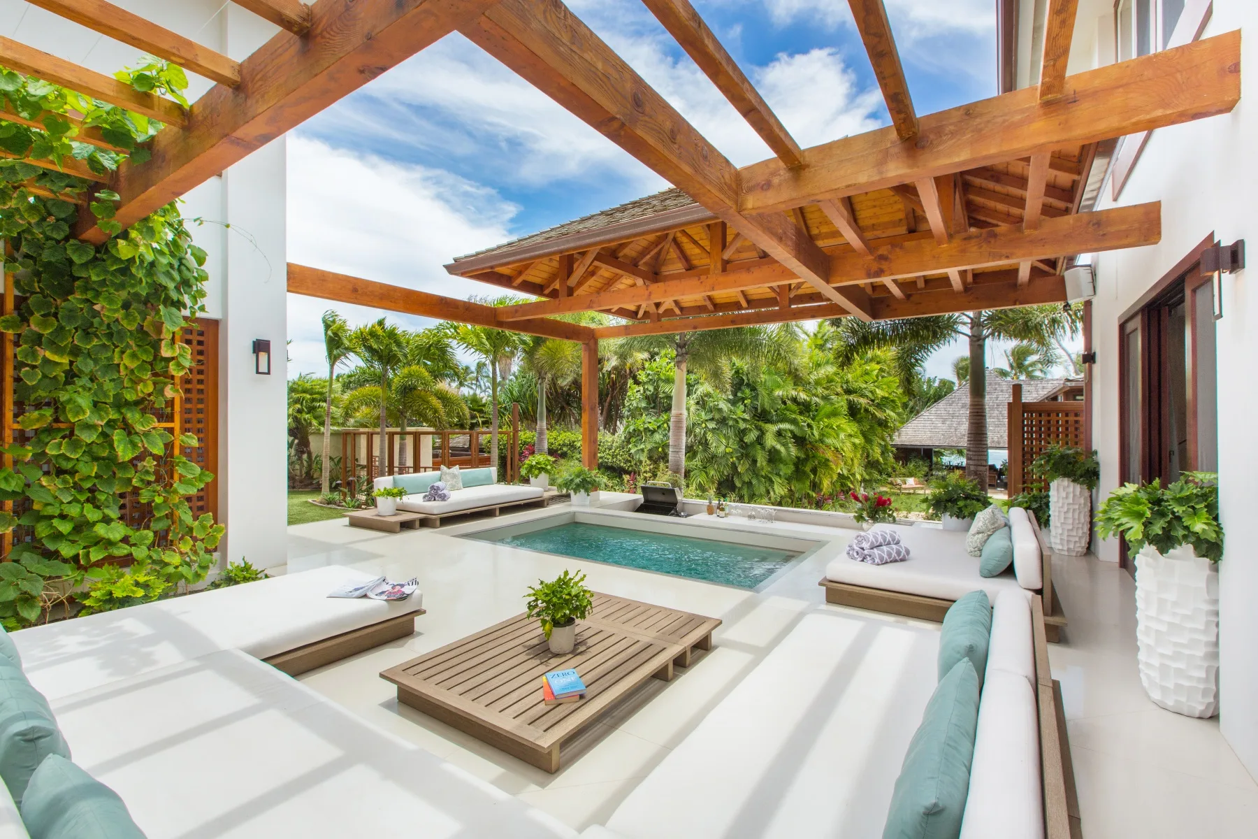 Una sala de estar al aire libre con una pequeña piscina, asientos bajos y una pérgola de madera.