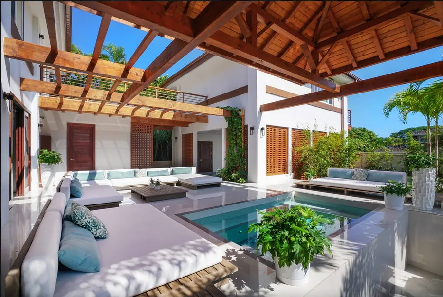 Una sala exterior cubierta rodea una piscina, con vigas de madera sobre ella.