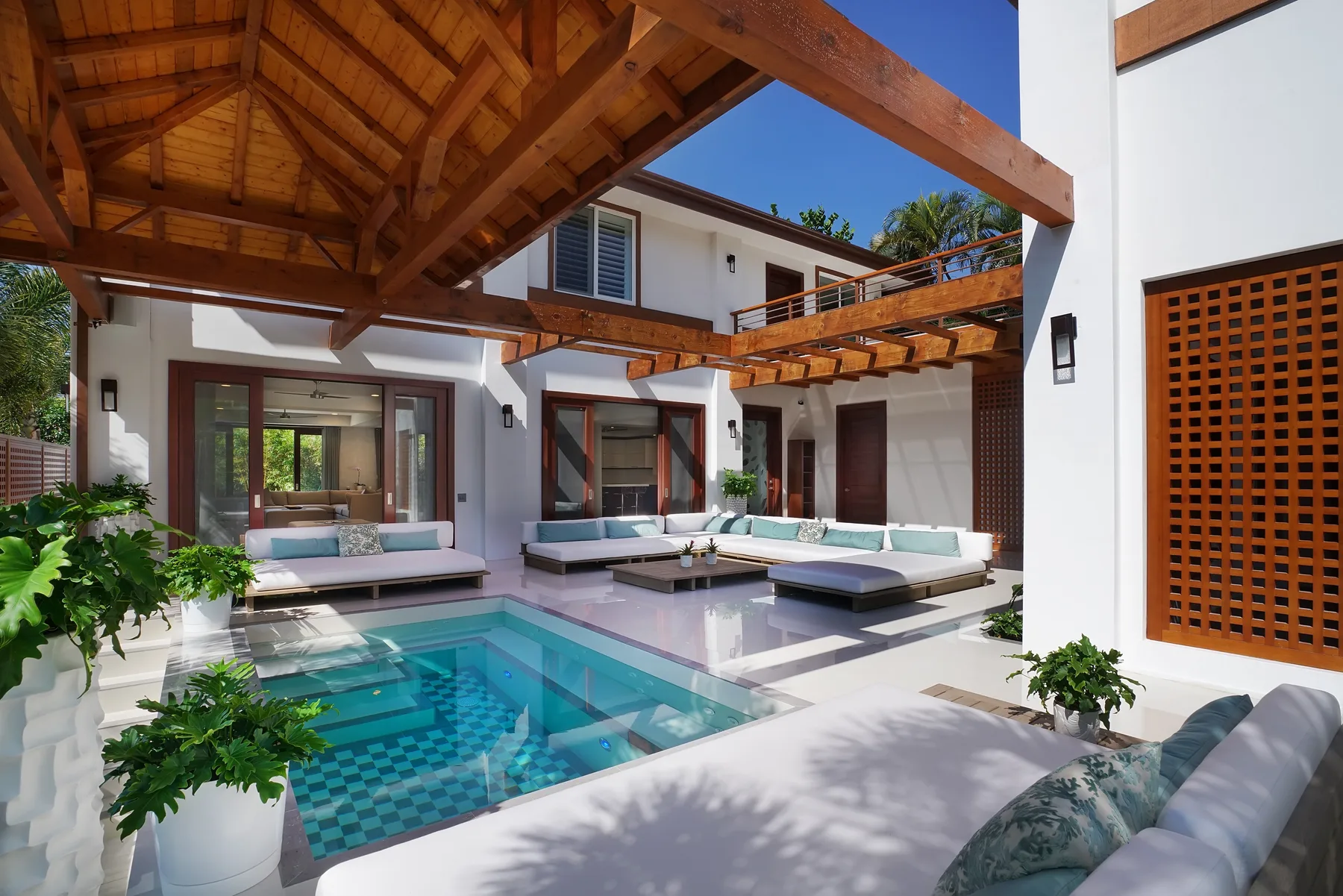 Un patio exterior con piscina y asientos bajo una pérgola de madera.