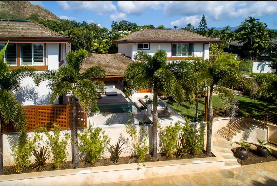 Una propiedad residencial tropical con edificios bajos, palmeras y un patio pavimentado.