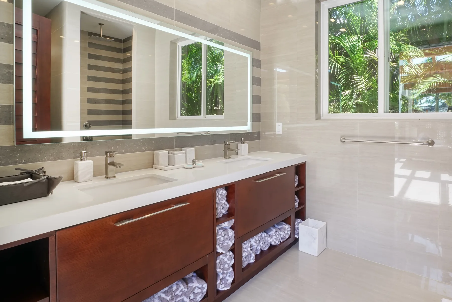 Un baño luminoso con un tocador largo, un espejo grande y ventanas con vistas a la vegetación.
