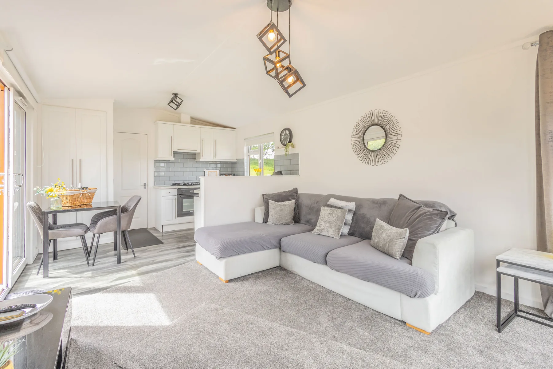 A bright living room with gray seating and a dining area beside the kitchen.