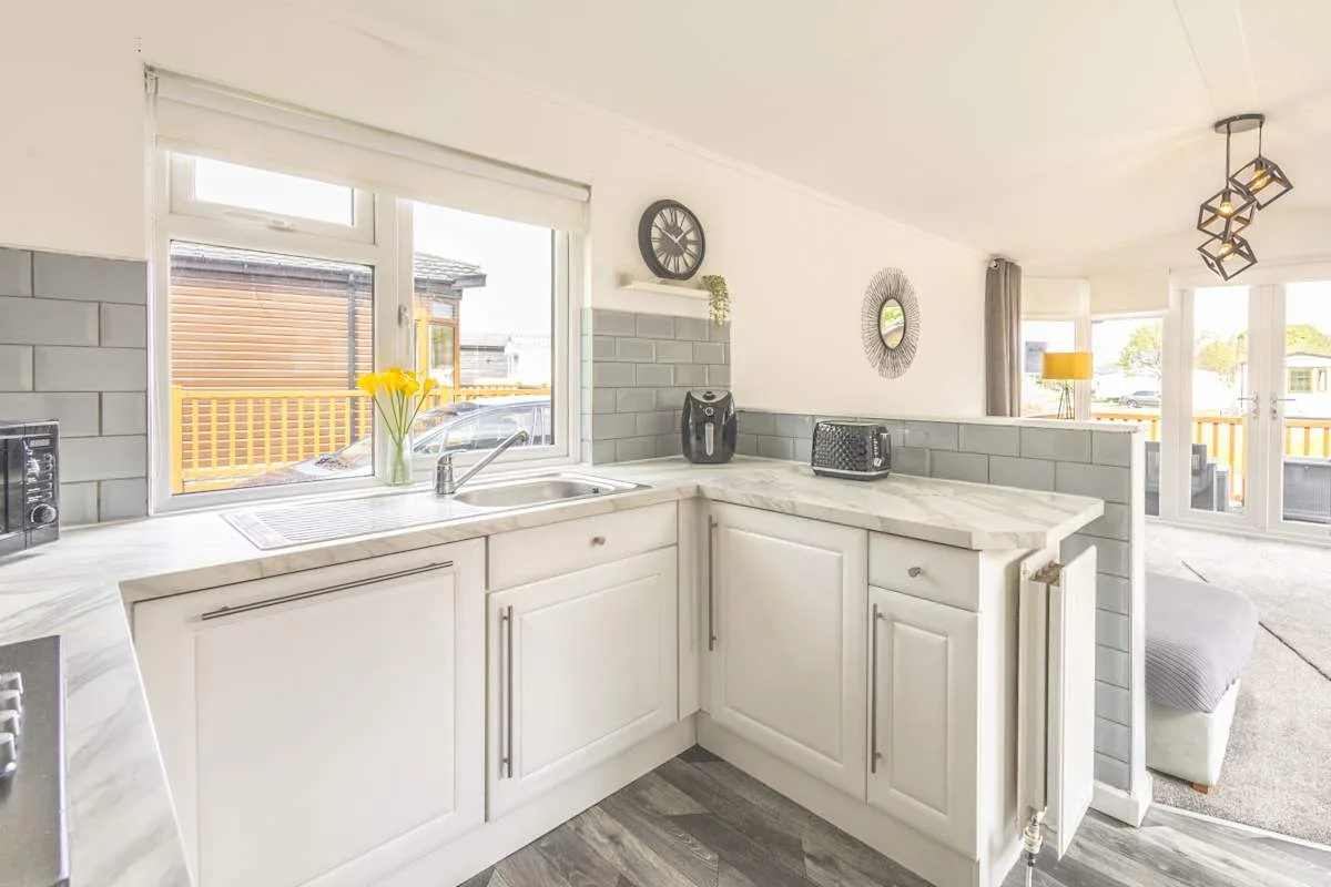 Una cocina luminosa con gabinetes blancos, paredes de azulejos y grandes ventanas.