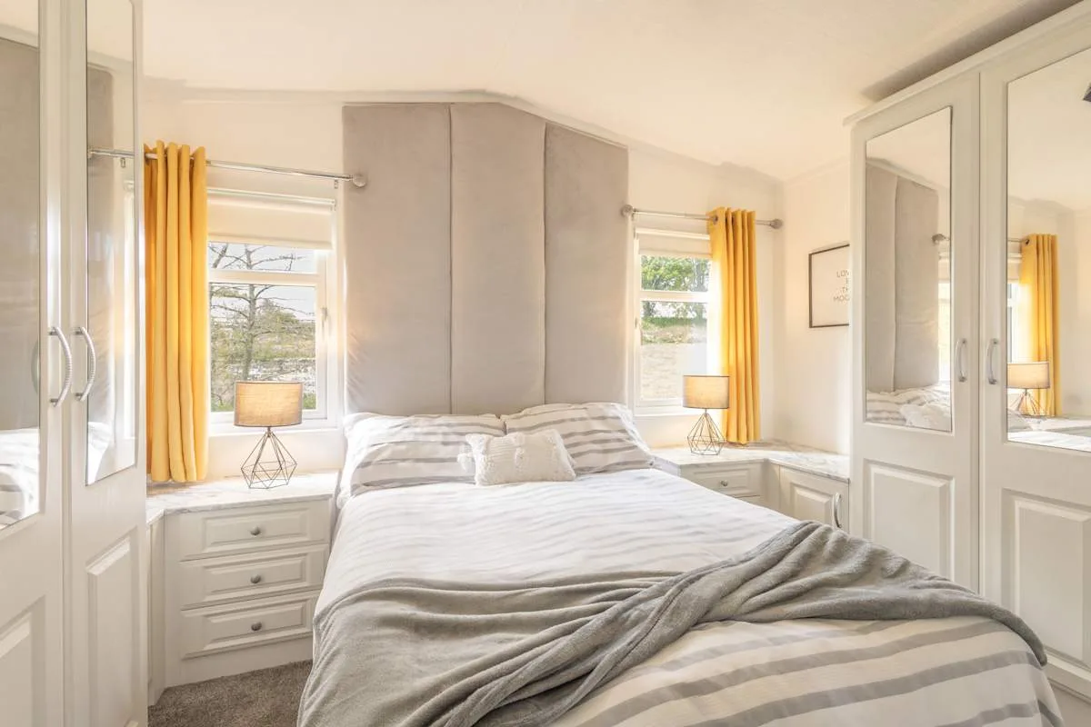 Un dormitorio luminoso con una cama, mesitas de noche y cortinas amarillas.