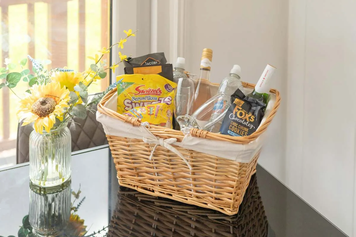 Una cesta con aperitivos y bebidas está sobre una mesa reflectante junto a unas flores.