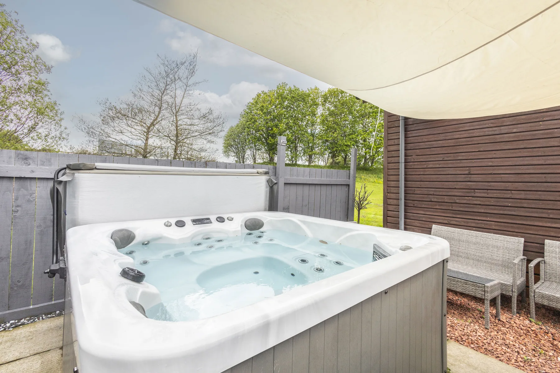 An outdoor hot tub sits beside a fenced patio beneath a shade canopy.