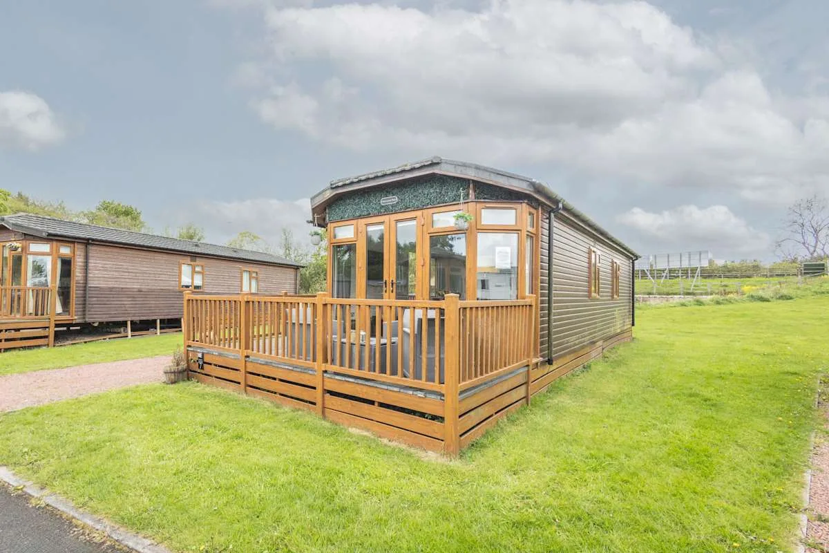 Una cabaña de madera con una terraza elevada está en un camping con césped.